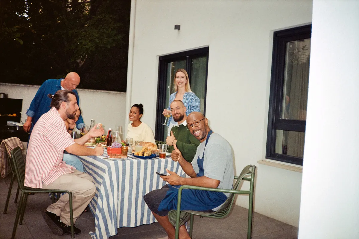 Three generations of a family sharing lunch at a long table on a sunny terrace