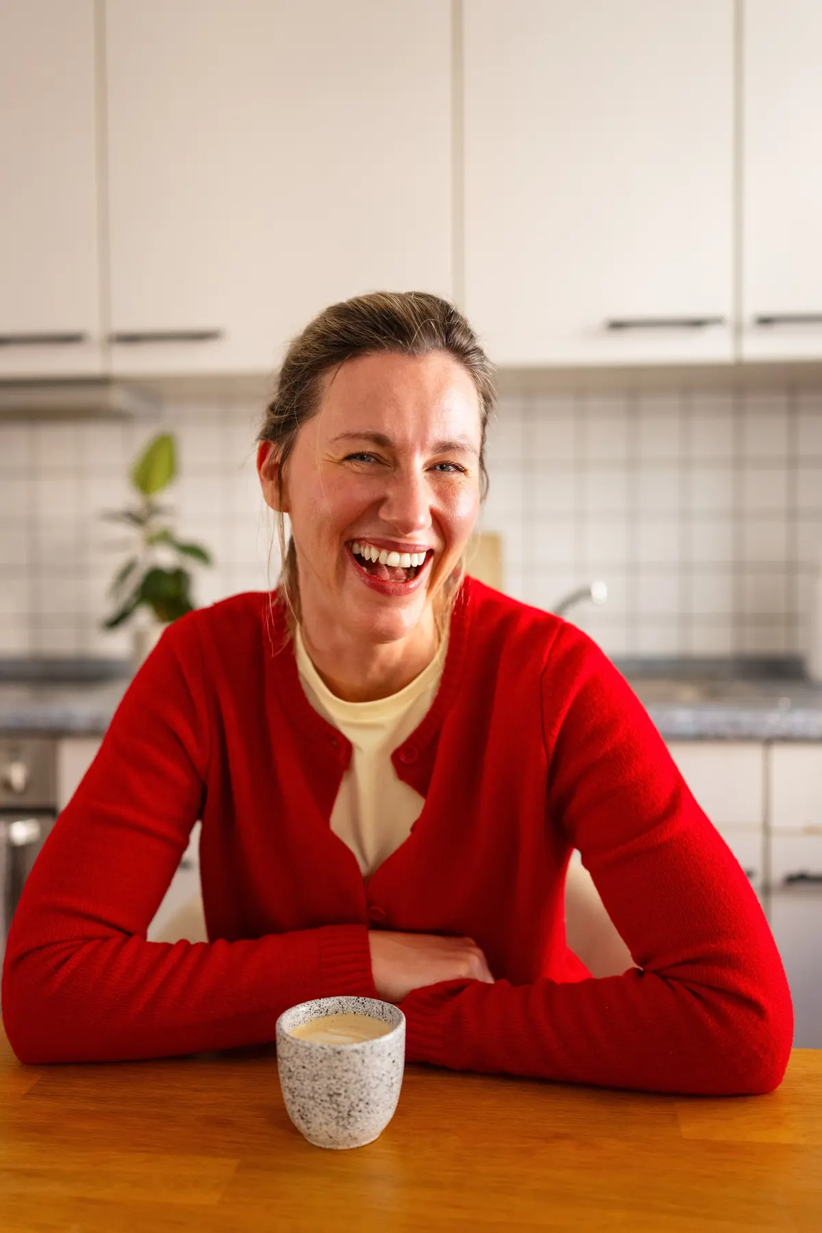 A woman laughing over her morning coffee at home
