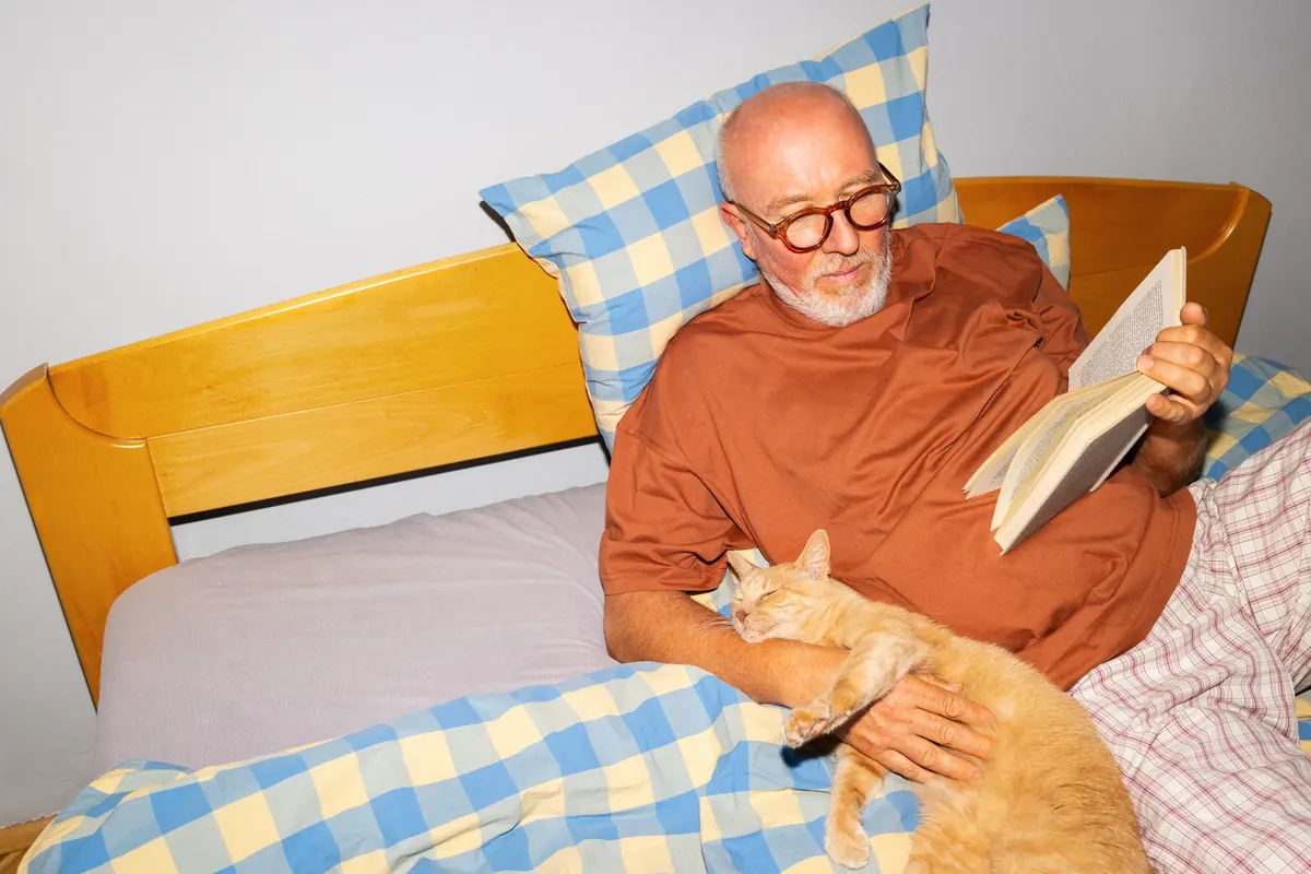 An older man relaxing in bed with a sleeping cat