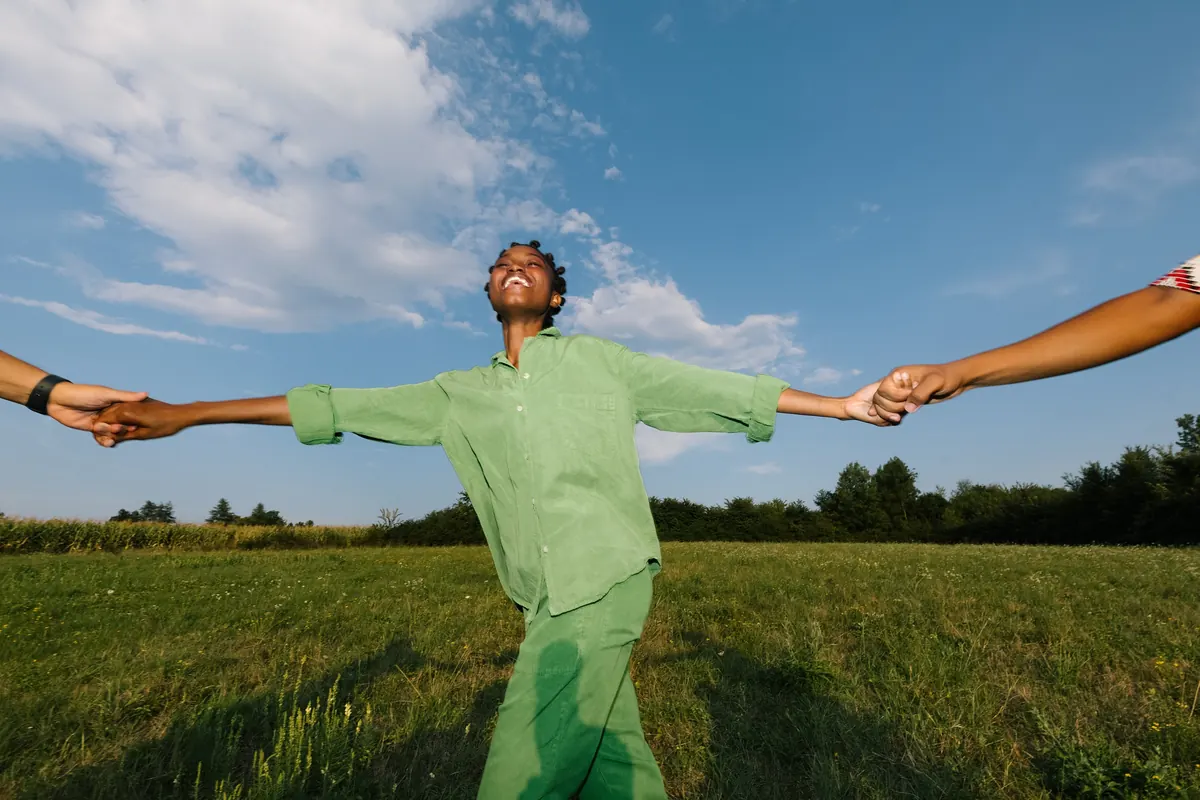 A man dancing freely in an open field under a blue sky