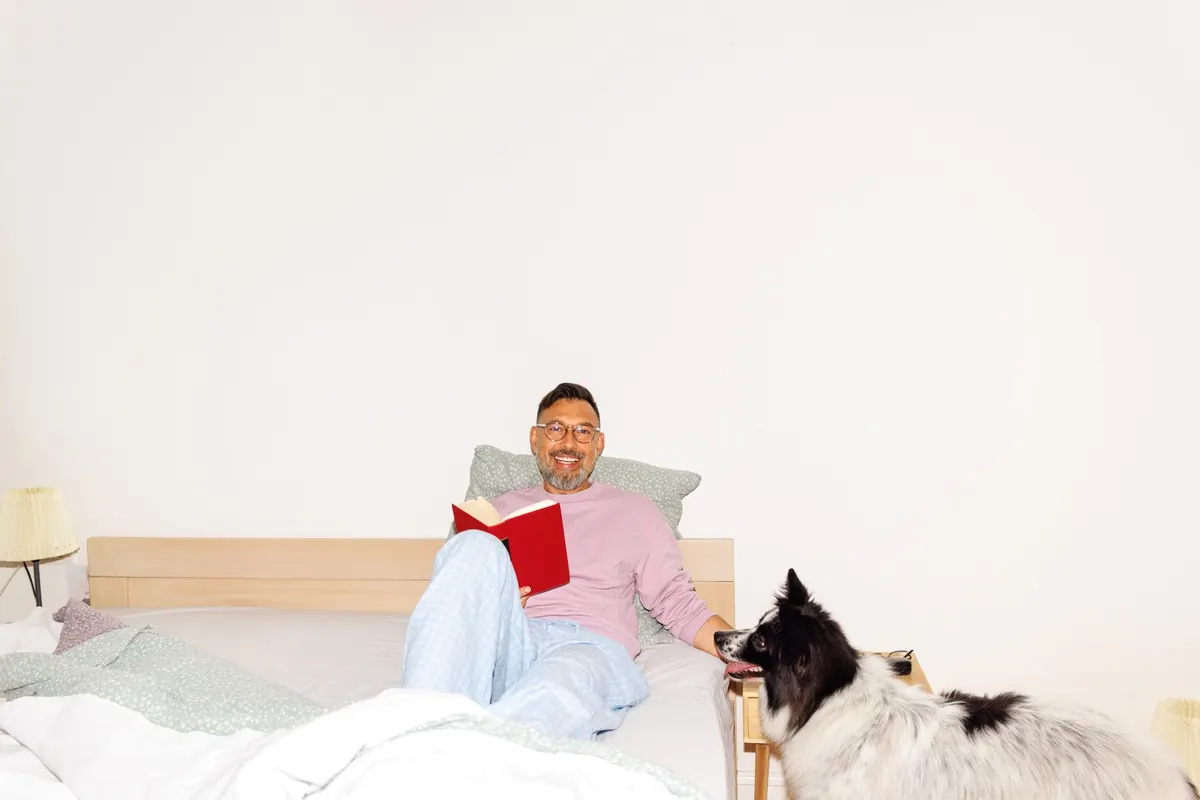 A person reading in bed with their dog curled up beside them